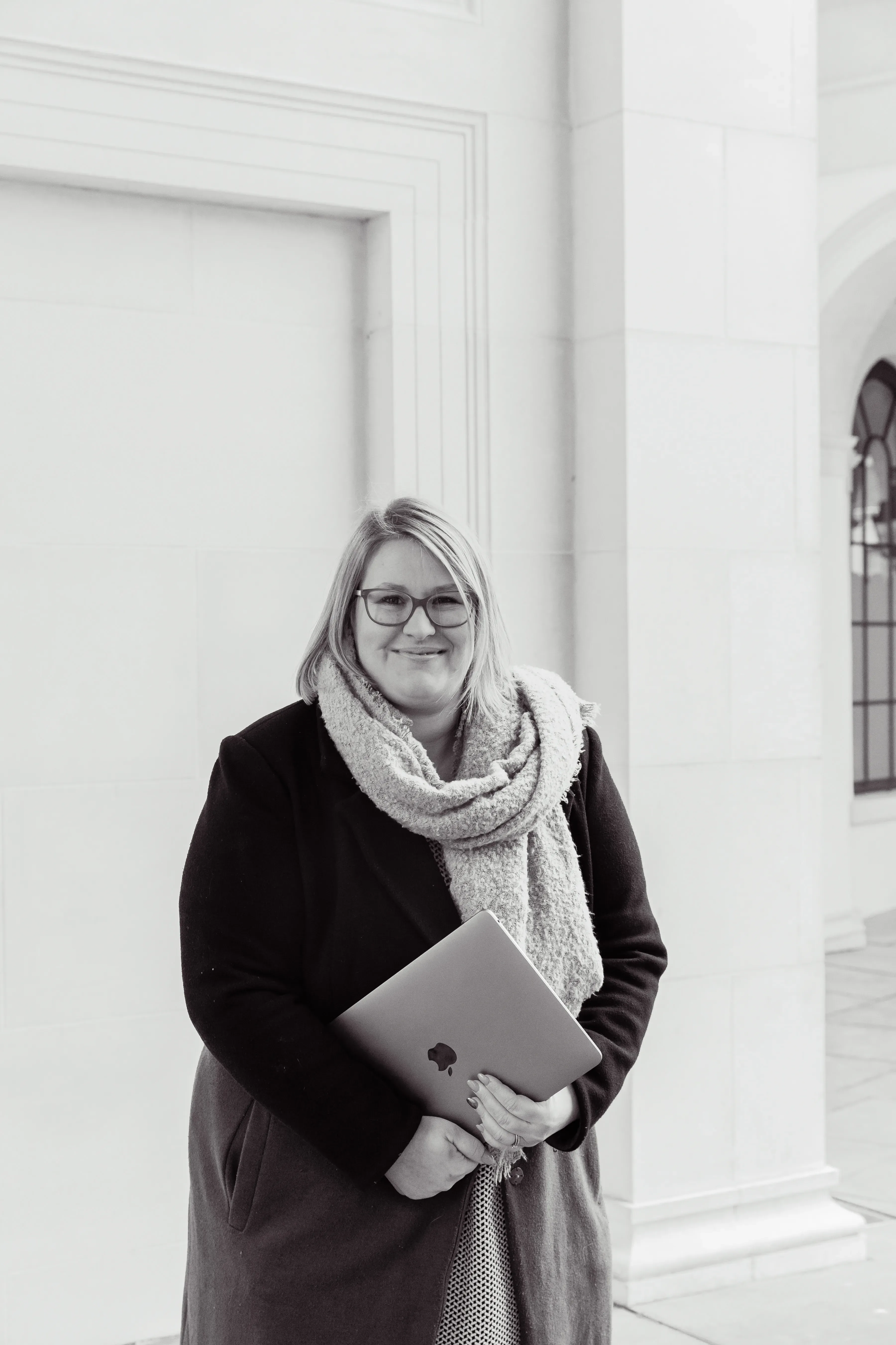 Gemma Hurlstone, founder of Calm Back with Gem, standing against a pale stone building, holding a laptop and smiling.