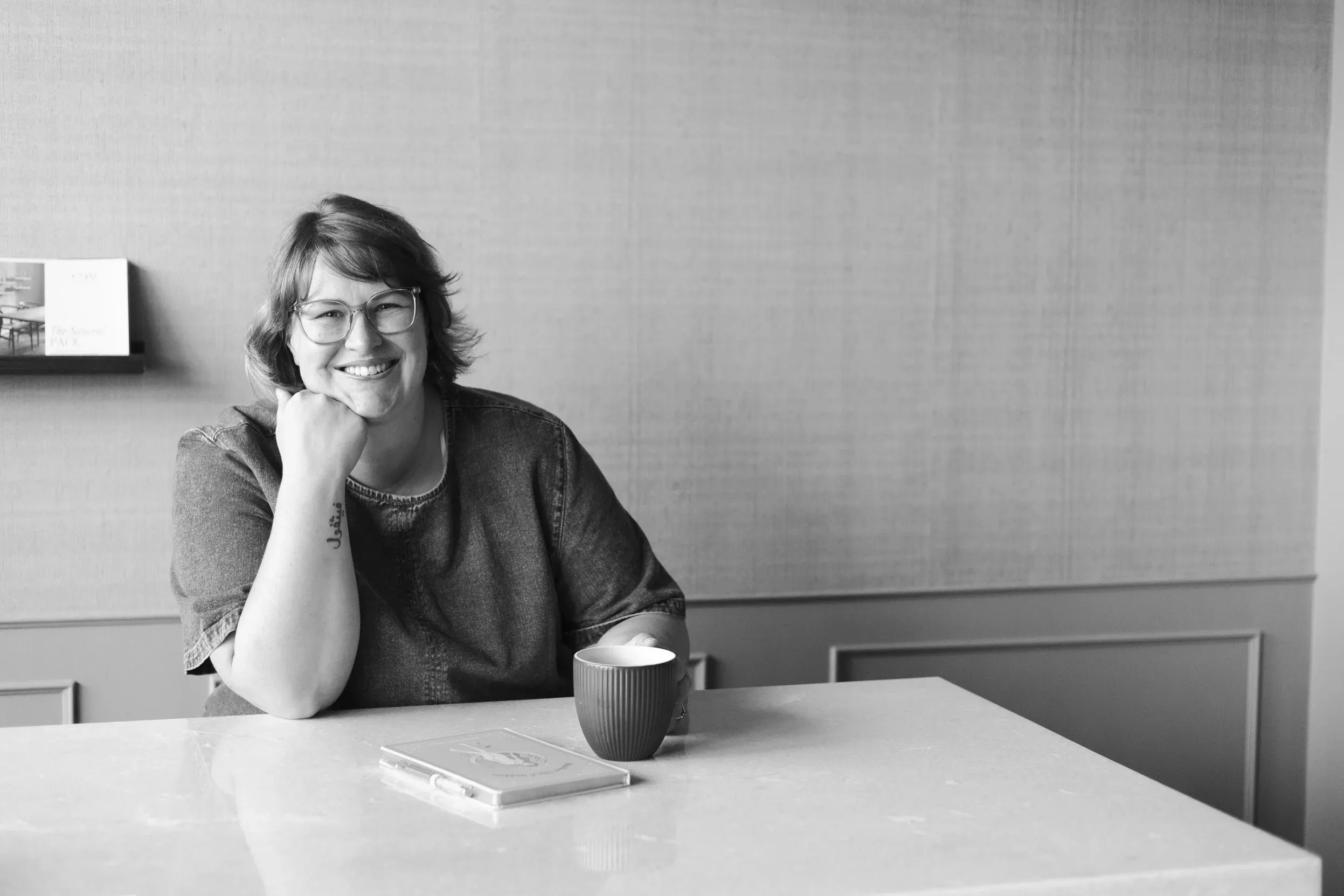 Gemma sitting at a table with a coffee, chin resting on her hand, listening.